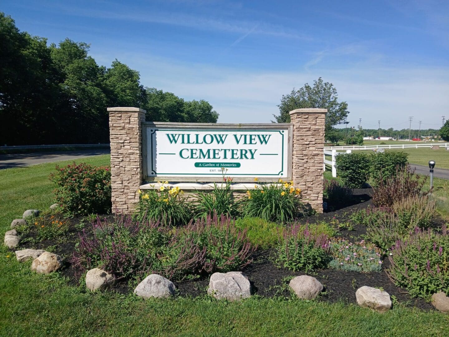 A sign for the willow view cemetery in front of some bushes